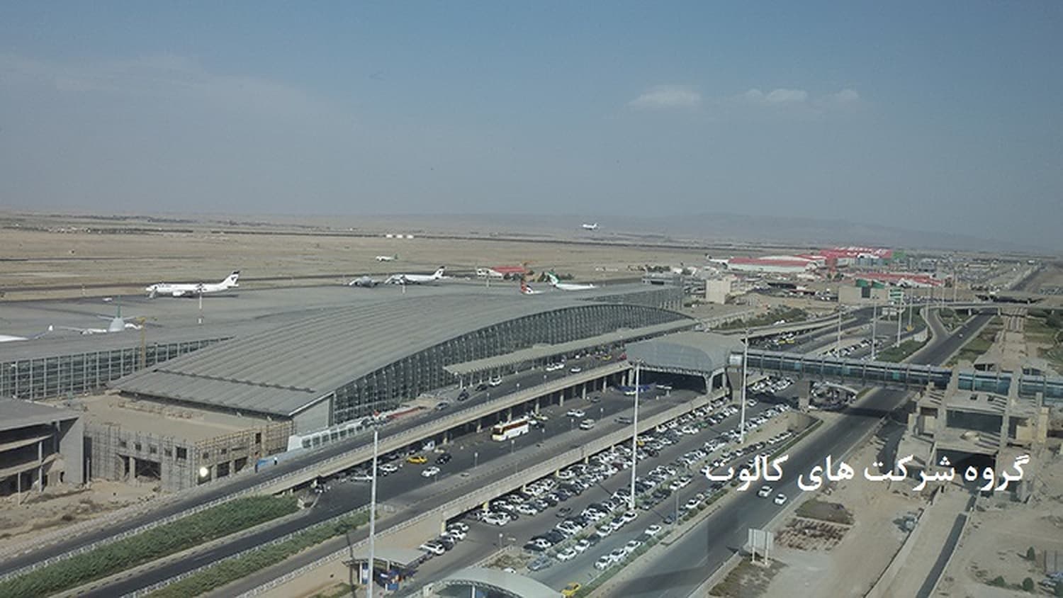 ترمینال فرودگاه با سقف فلزی و هواپیماهای روی اپرون در پس‌زمینه