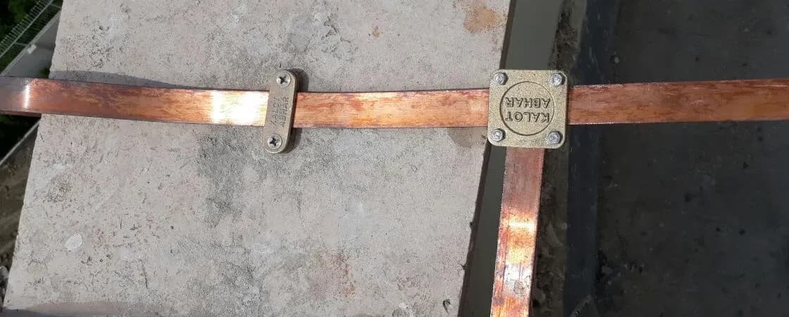 تسمهٔ مسی روی جان‌پناه بام با بست برنجی دوپارچهٔ دیواری و بست مربعی برنجی کالوت در محل انشعاب تسمه