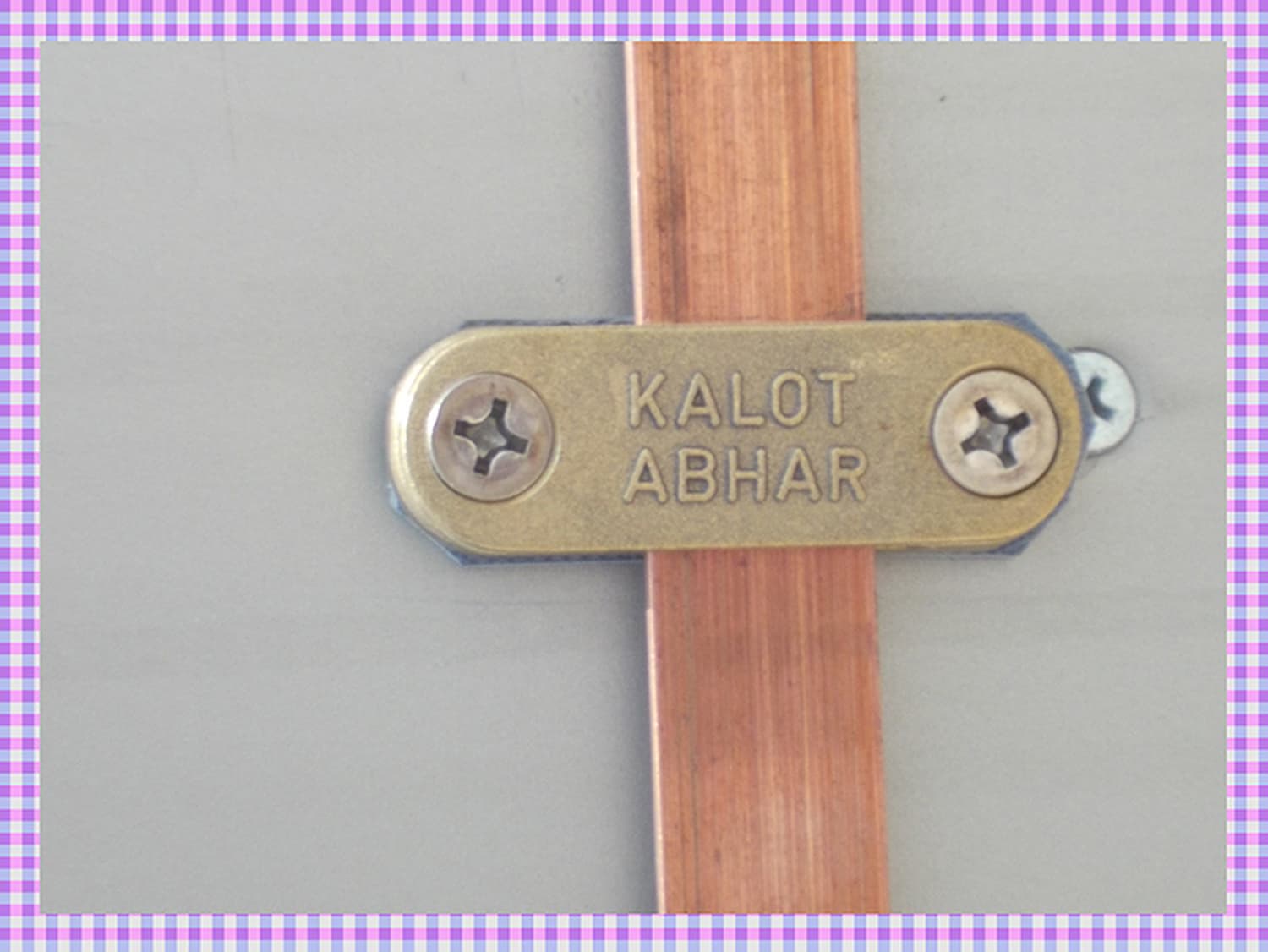 بست برنجی دوپیچ با نشان برجستهٔ KALOT ABHAR که تسمهٔ مسی را روی سطح نگه می‌دارد