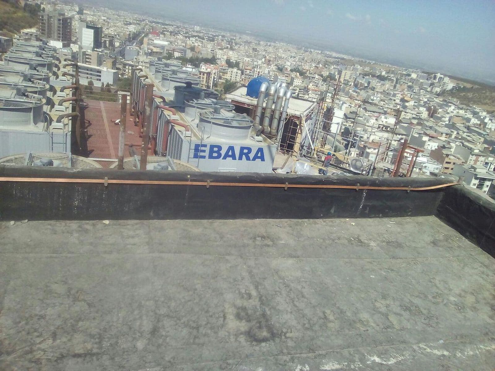 هادی مسی روی جان‌پناه بام مشرف به ساختمان‌های صنعتی و شهر
