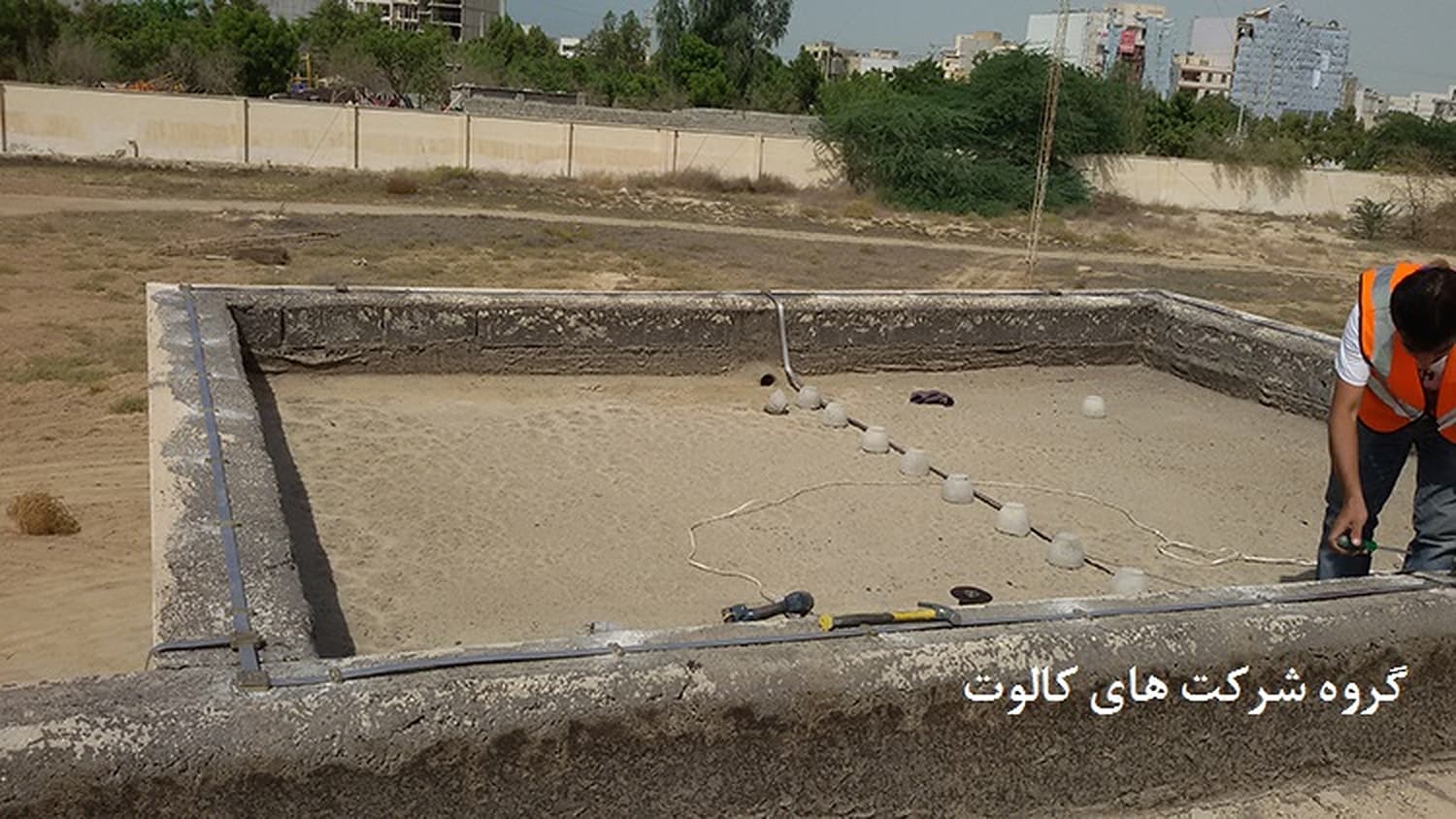 تکنسین با جلیقهٔ نارنجی کنار چالهٔ مستطیلی آماده‌شده برای شبکهٔ زمین