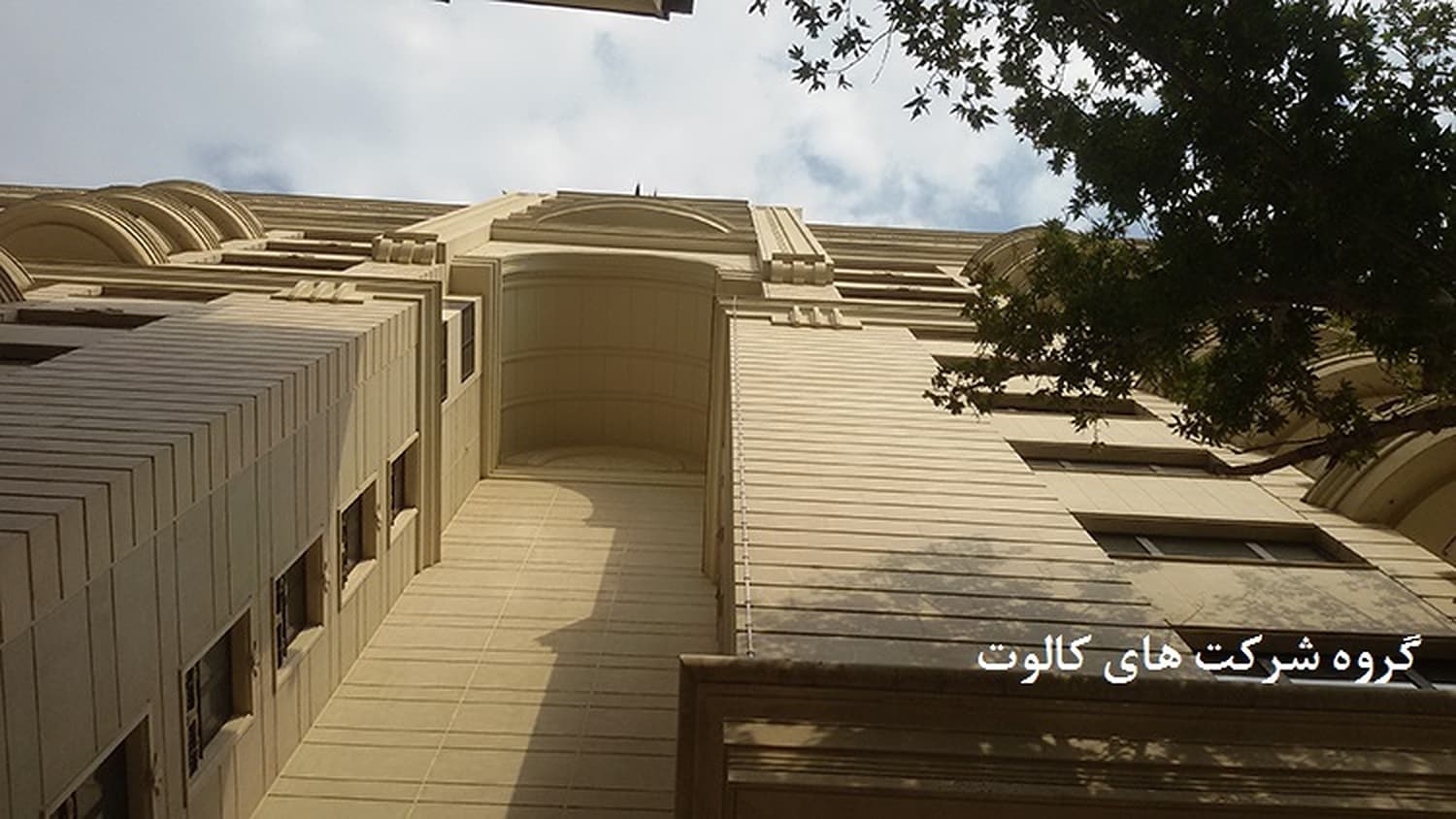 نمای سنگی ساختمان مسکونی از زاویهٔ پایین با شاخه‌های درخت