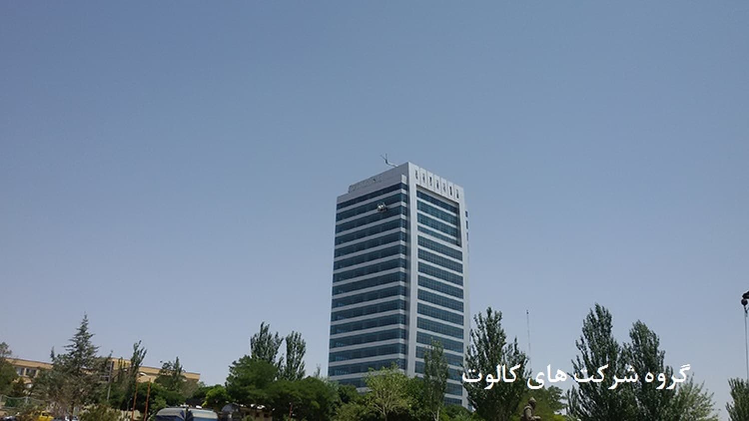 برج اداری با نمای شیشه‌ای آبی میان درختان